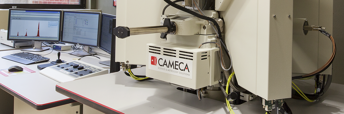 Close-up of a Cameca SXFive electron probe microanalyzer with computer monitors displaying elemental analysis data and instrument controls.
