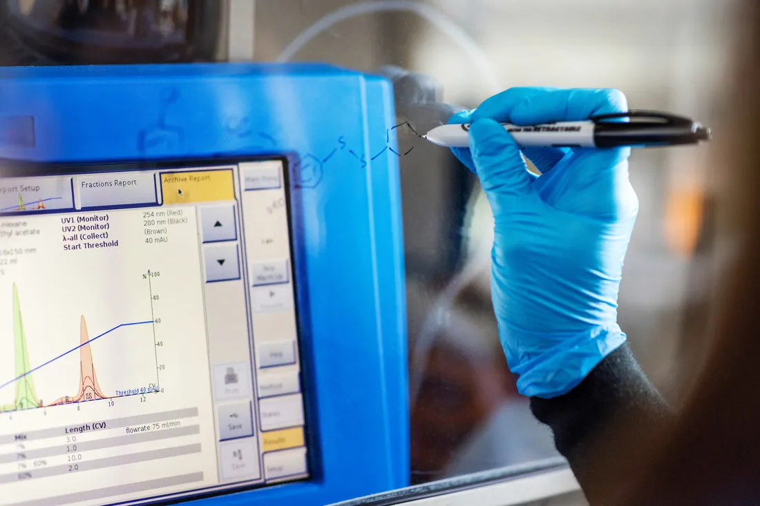 Gloved hand writes equation on screen.