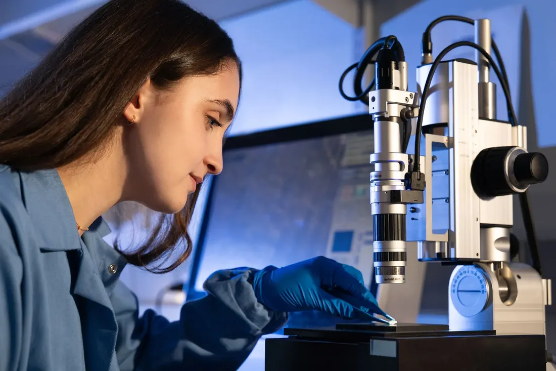 Scientist in laboratory adjusts sample on microscope.