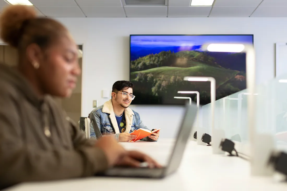 Two people in shared working space working on laptops on table.
