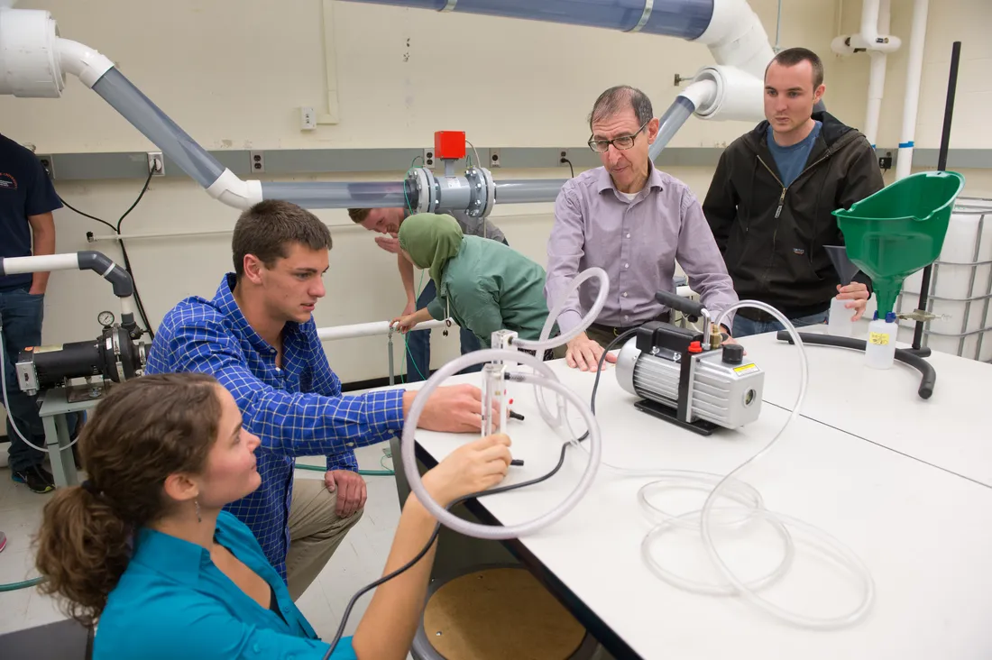 Four researchers gather around table in lab looking at lab equipment.