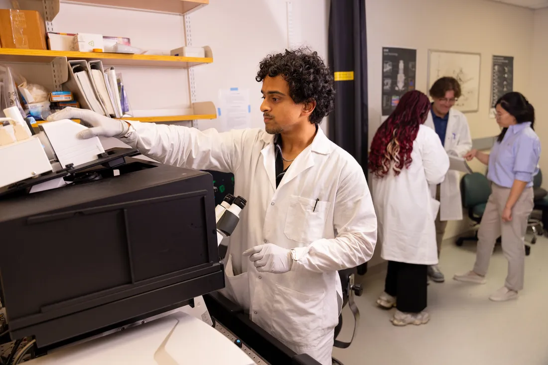 Man in lab coat adjusts input in machine in laboratory.