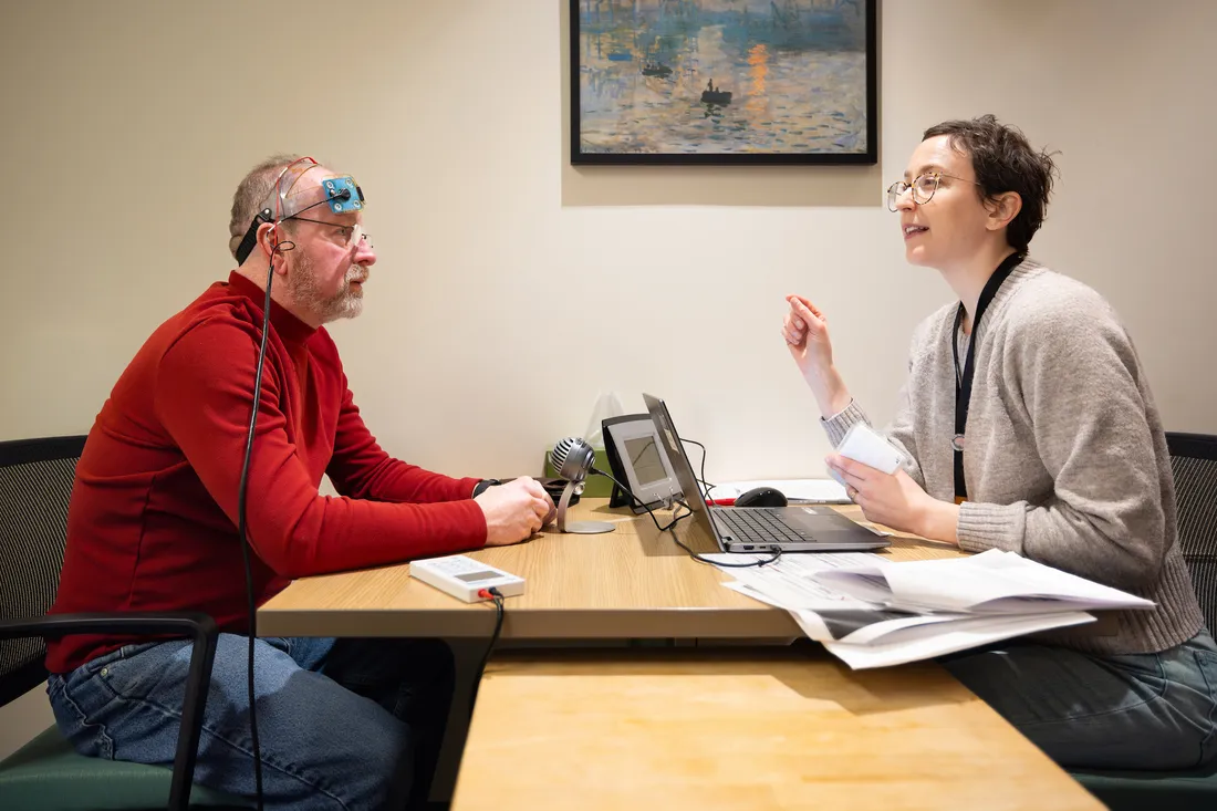 A researcher meets one-on-one with a participant across a desk, discussing documents during an informed consent or research study consultation.