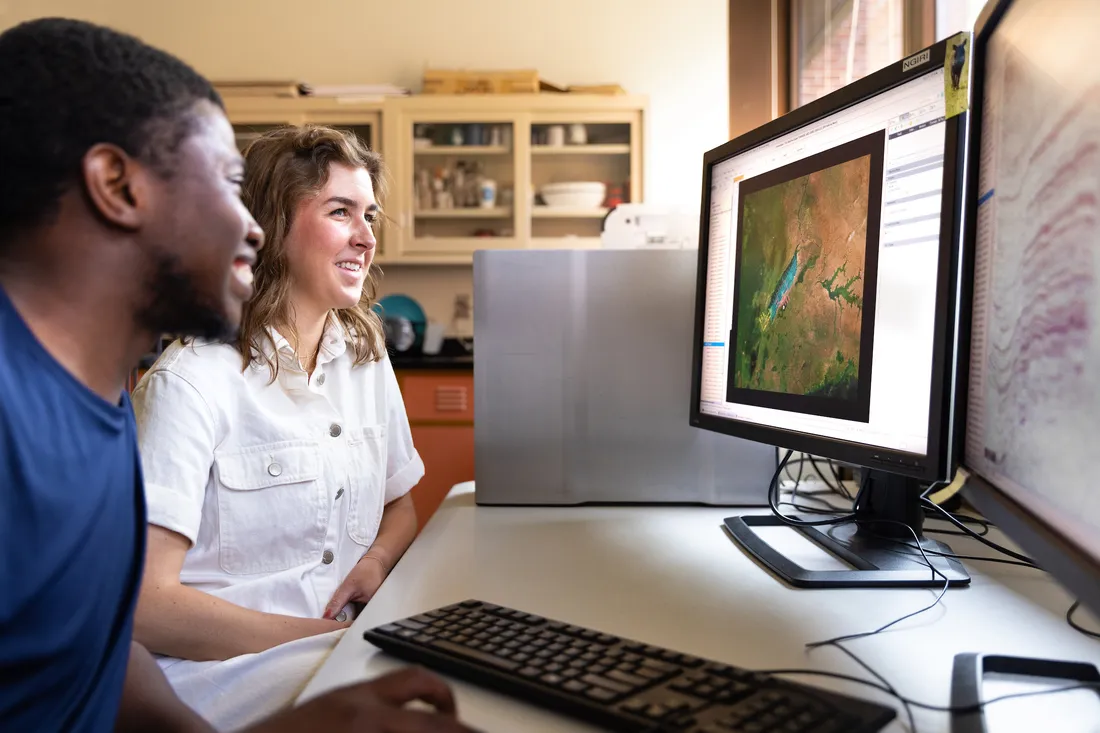 Two researchers sit in front of computer looking at topographical image on monitor.